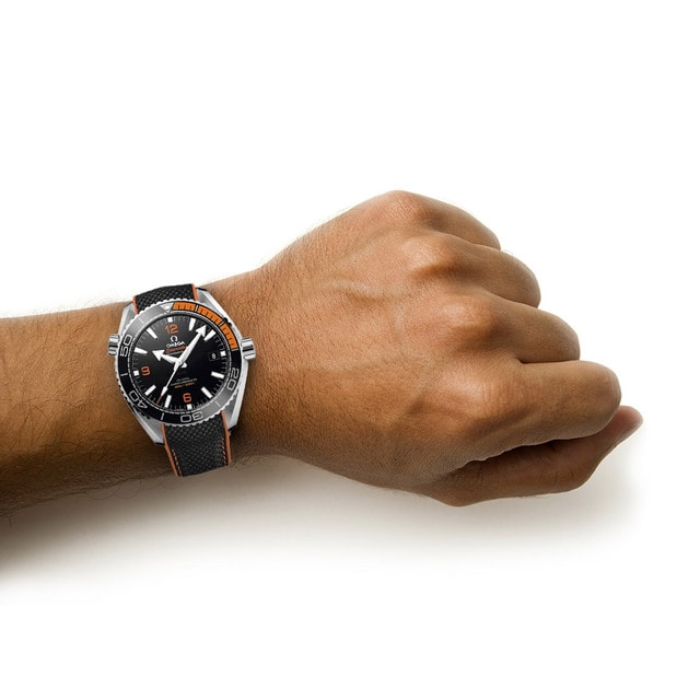 A person’s left wrist wearing a black and orange OMEGA Seamaster Planet Ocean 600M dive watch on a white background.