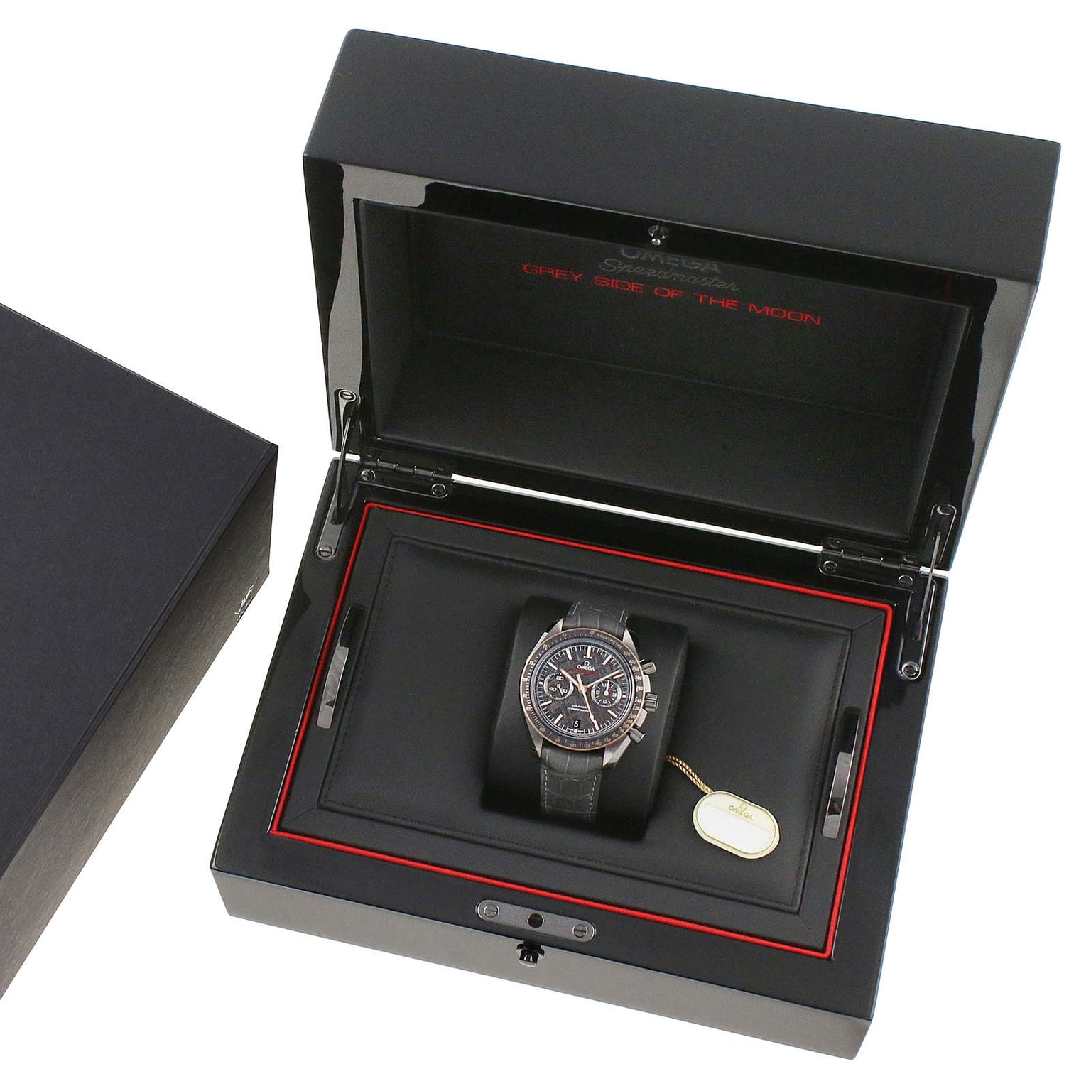 The OMEGA Speedmaster Dark Side of the Moon Meteorite luxury wristwatch, featuring a black strap and sleek ceramic case, is displayed in an open black presentation box with a removable tag beside it.