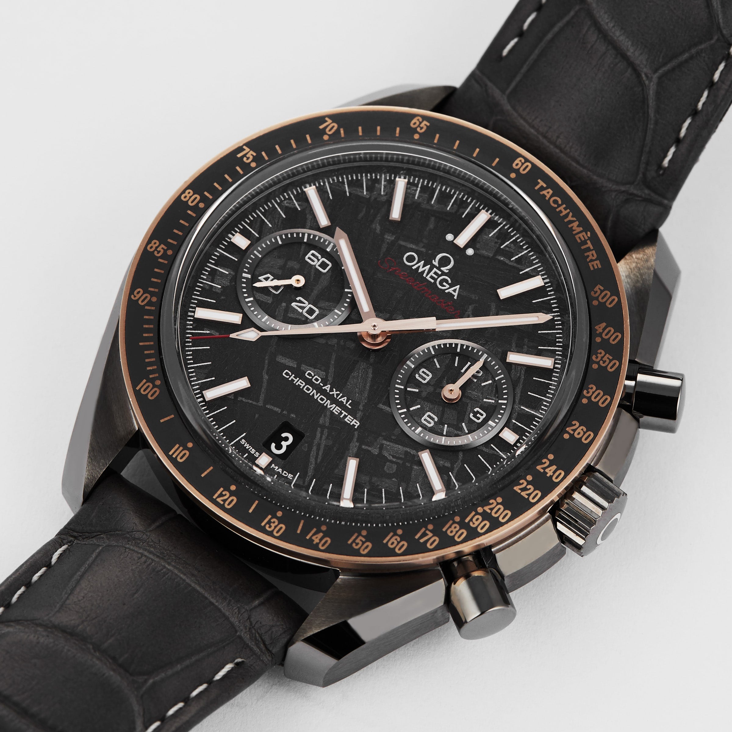 A close-up of the OMEGA Speedmaster Dark Side of the Moon Meteorite, showcasing its ceramic case, black leather strap, black and gold-accented dial with three subdials and a date window at 6 o’clock.