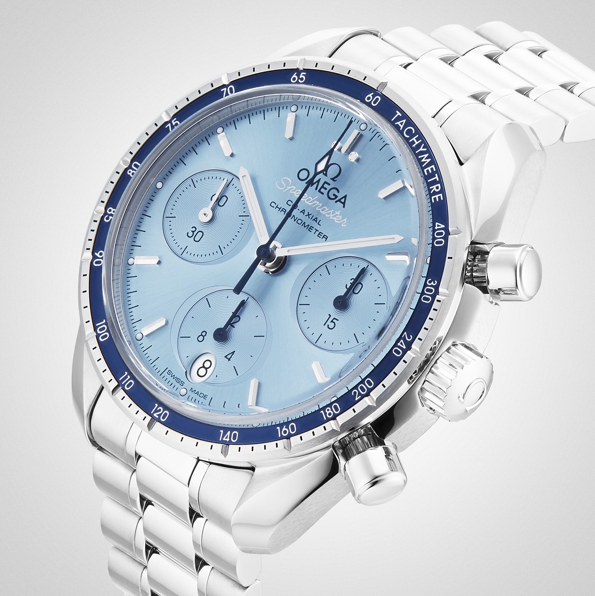 The OMEGA Speedmaster 38 is a stainless steel chronograph wristwatch featuring a light blue dial with three sub-dials, date display, and tachymeter bezel on a metal bracelet, powered by the precise 3330 calibre movement.