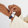 A person in a light-colored blazer adjusts an OMEGA De Ville Tresor 36, a luxury timepiece with a blue strap and white face.