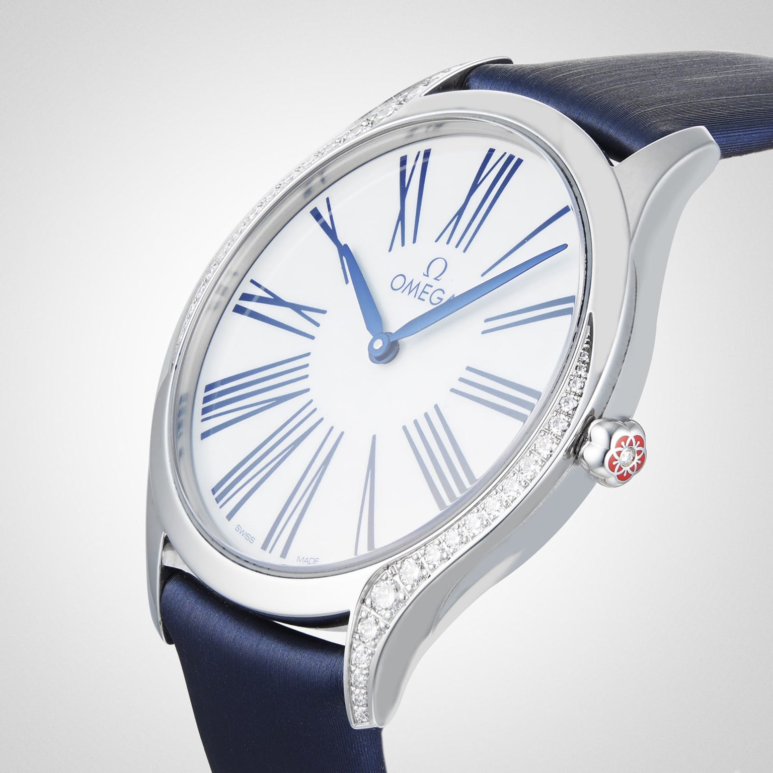 The OMEGA De Ville Tresor 36 ladies watch, featuring a silver case, white dial with blue Roman numerals and hands, diamond-set bezel, and blue strap, is elegantly displayed on a light background.