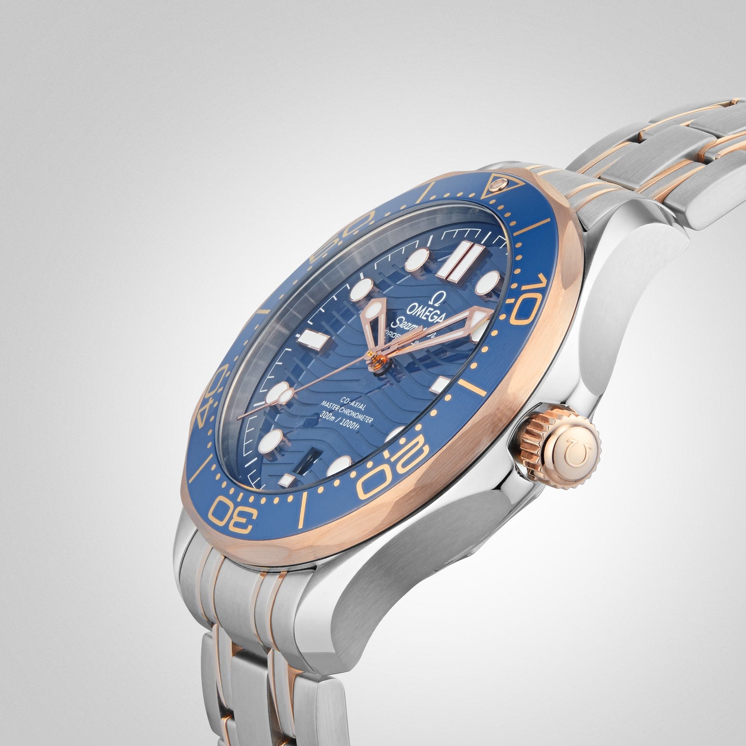 A close-up of the OMEGA Seamaster Diver 300M wristwatch, featuring a blue face, gold accents, and a silver-gold metal band, inspired by James Bond, set against a light gradient background.