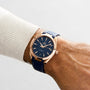 An individual wears an OMEGA Seamaster Aqua Terra 150M with a gold case, blue dial, and blue strap on their left wrist, the watch partly visible under a light-colored sweater sleeve.