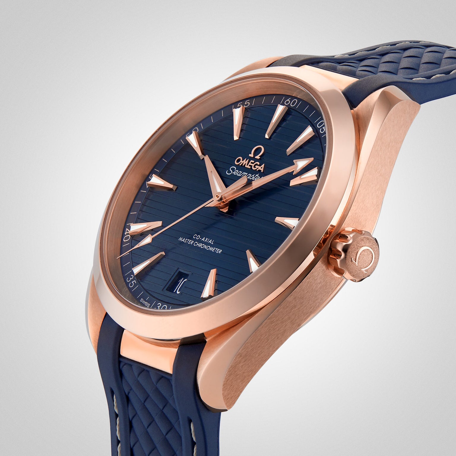 A close-up of the OMEGA Seamaster Aqua Terra 150M shows its rose gold case, blue dial, and textured blue strap, highlighting its Master Chronometer certification against a plain light background.