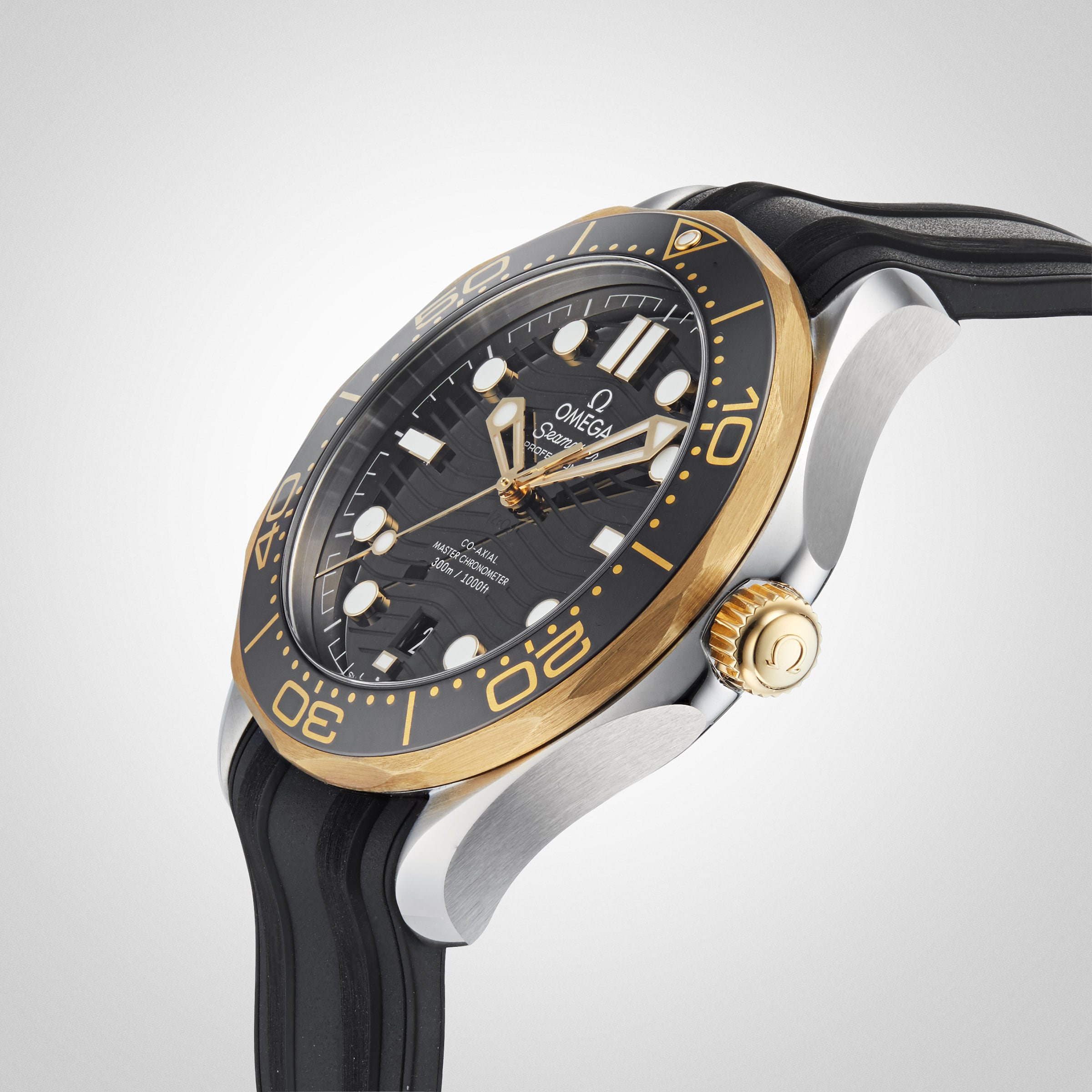 The OMEGA Seamaster Diver 300M, shown at an angle on a light gradient background, features a black dial, gold bezel, and black rubber strap, powered by the Co-Axial calibre 8800 Master Chronometer.