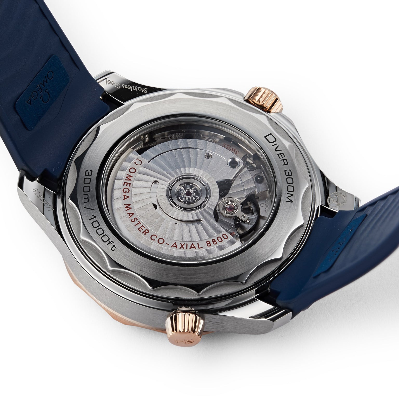 A close-up of the OMEGA Seamaster Diver 300M case back shows the OMEGA MASTER CO-AXIAL 8800 movement, blue strap, and 300m / 1000ft water resistance.