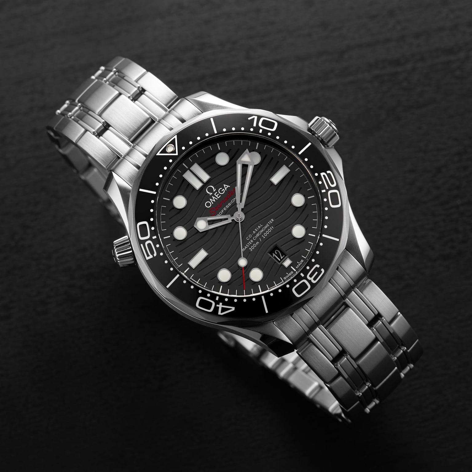 An OMEGA Seamaster Diver 300M wristwatch with a stainless steel bracelet, black dial, and white markers is displayed on a dark surface.