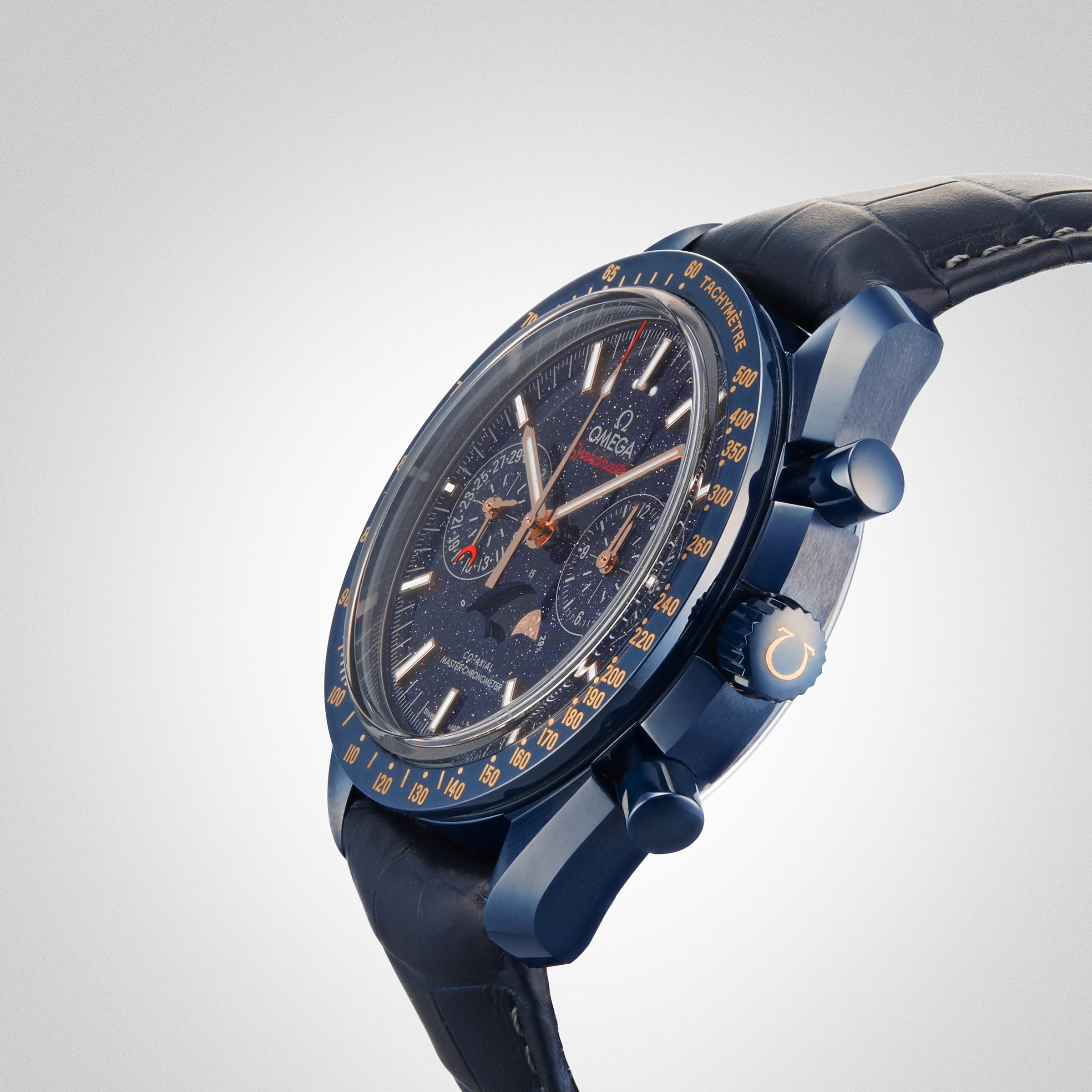 A blue OMEGA Speedmaster 44 Ceramic wristwatch with a dark dial, multiple sub-dials, gold accents, and a leather strap is displayed against a plain white background.