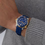 A person in a gray sweater showcases an OMEGA Seamaster Diver 300M wristwatch with a blue and gold case, blue rubber strap, blue dial, and powered by the advanced 8800 calibre movement.