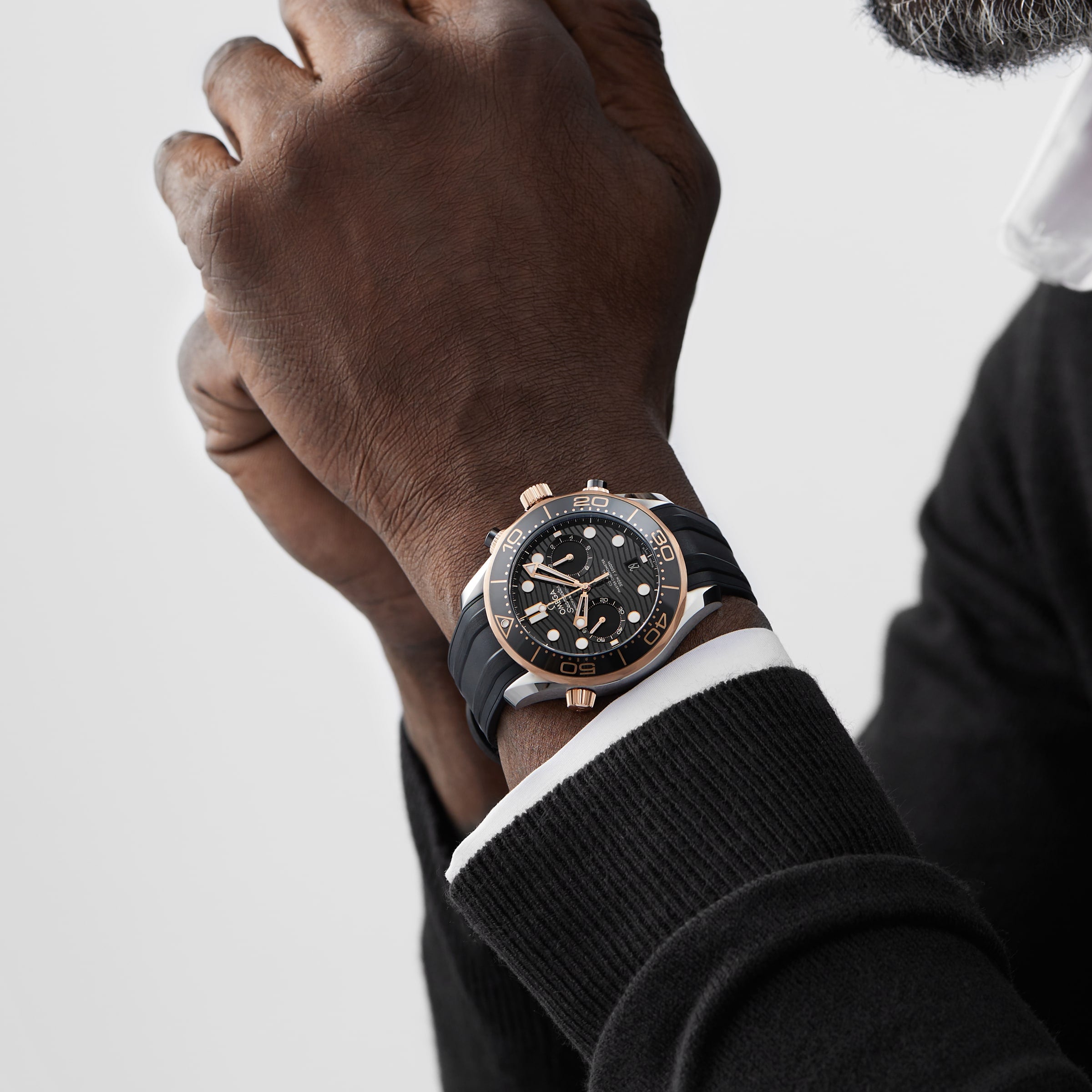 Someone wearing the OMEGA Seamaster Diver 300M in black and rose gold with a black strap, paired with a black sweater and white shirt cuff—evoking classic James Bond watch style.