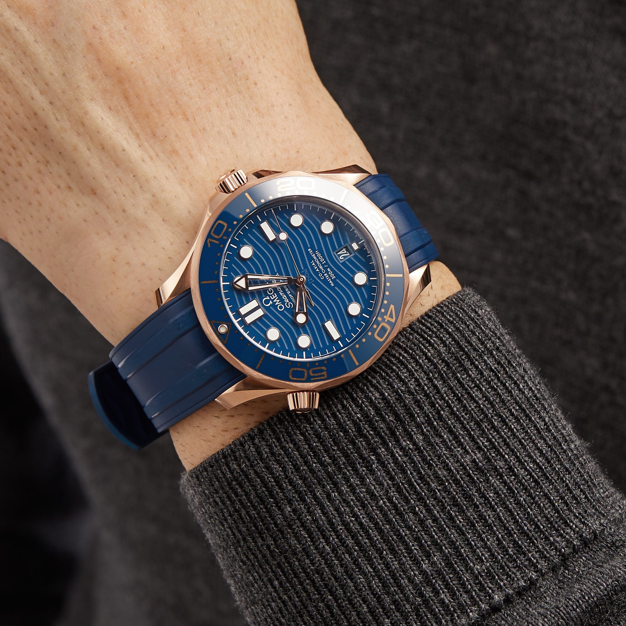 Someone wears an OMEGA Seamaster Diver 300M with a blue and rose gold case and blue rubber strap, reminiscent of the iconic timepieces worn by James Bond.