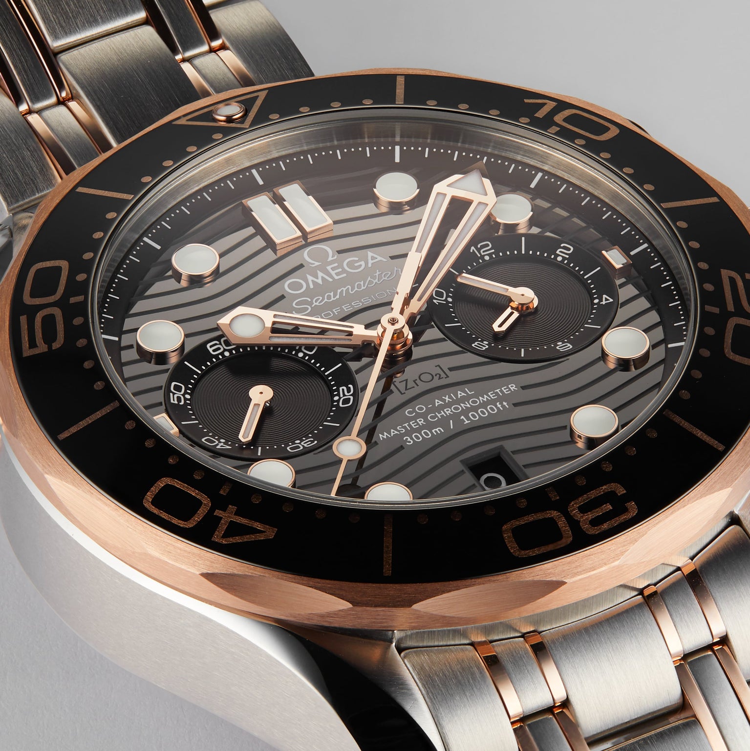 Close-up of an OMEGA Seamaster Diver 300M wristwatch with a black and gold bezel, black dial, silver and 18K Sedna™ gold bracelet, and multiple subdials.