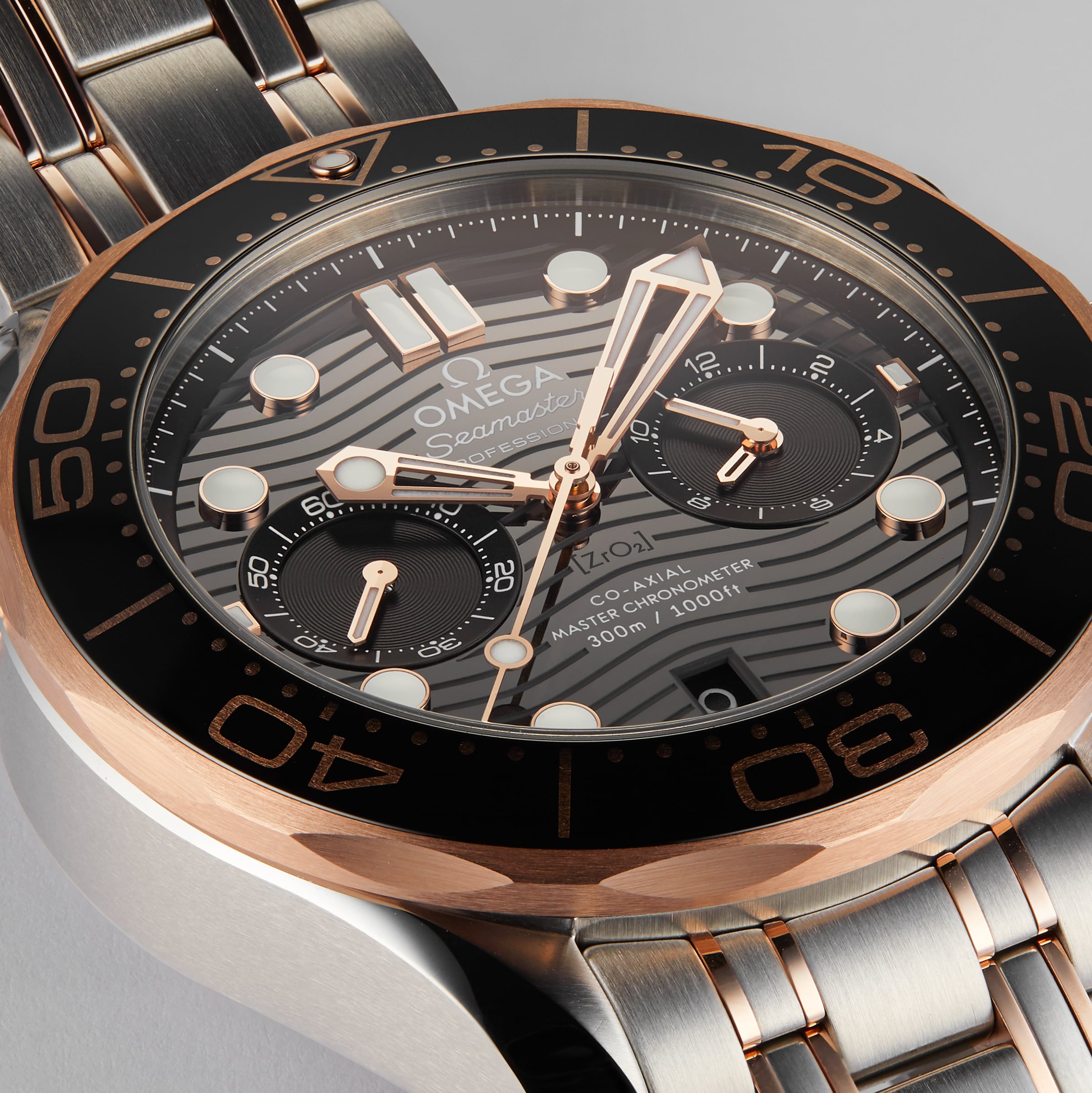 Close-up of an OMEGA Seamaster Diver 300M wristwatch with a black and gold bezel, black dial, silver and 18K Sedna™ gold bracelet, and multiple subdials.