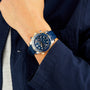 A person in a navy jacket and gray shirt wears an OMEGA Seamaster Diver 300M with a blue dial and blue strap.