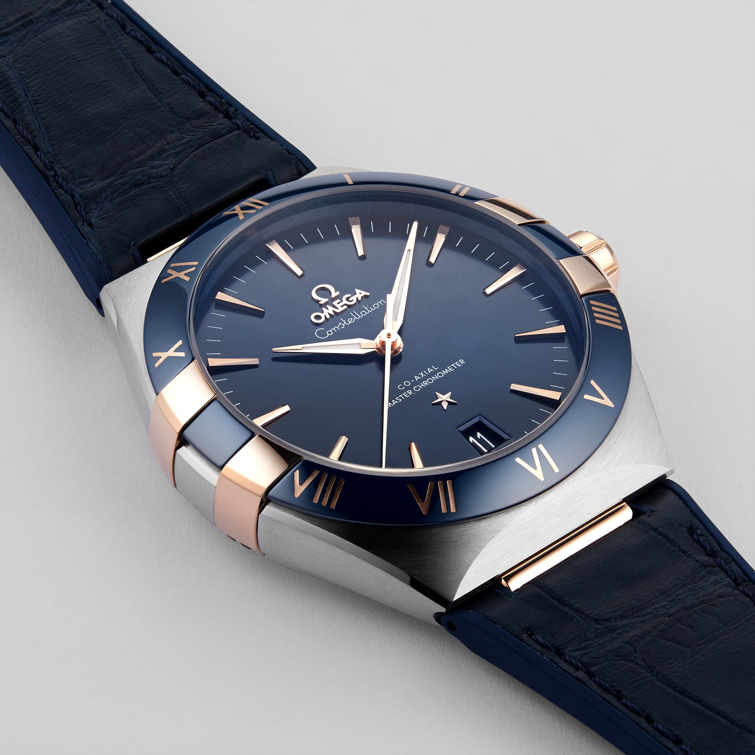 A close-up of the OMEGA Constellation wristwatch, featuring a blue dial, blue leather strap, and gold accents, showcases its Master Chronometer precision at 10:08.
