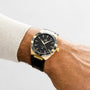 A wrist wears an OMEGA Constellation watch in gold and black with Roman numerals on a black leather strap, showcased against a plain background.