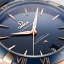 Close-up of an OMEGA Constellation watch featuring a blue dial, Sedna™ gold hands and markers, and a date window showing 8—honoring its iconic Constellation heritage.