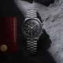 An OMEGA Speedmaster Moonwatch Professional with a black dial sits on a textured gray surface next to its red Master Chronometer certification card.