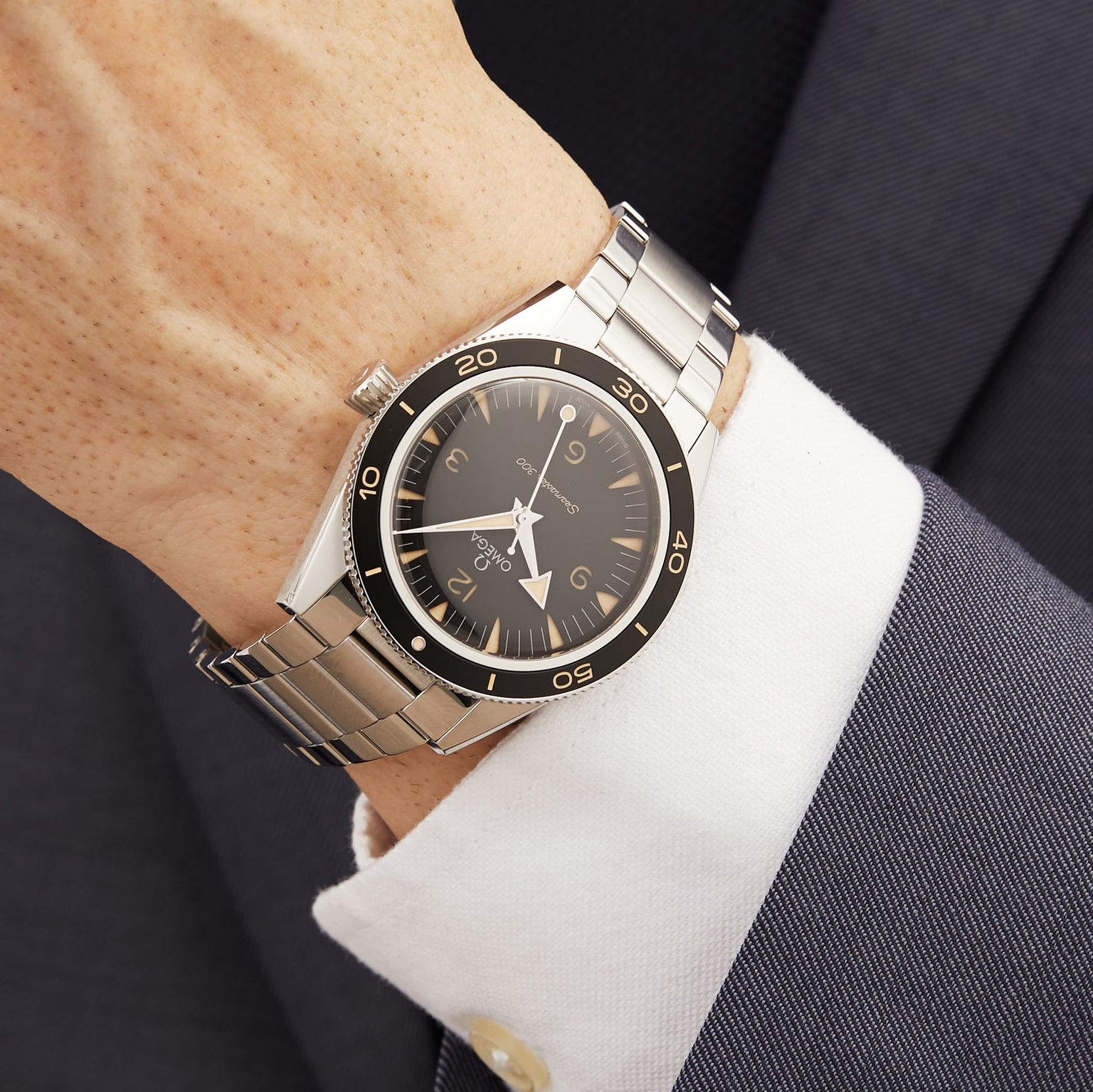 A close-up of a wrist wearing the OMEGA Seamaster 300, featuring a black bezel and dial, powered by the Co-Axial Master Chronometer Calibre 8912, paired with a white shirt and dark suit jacket.