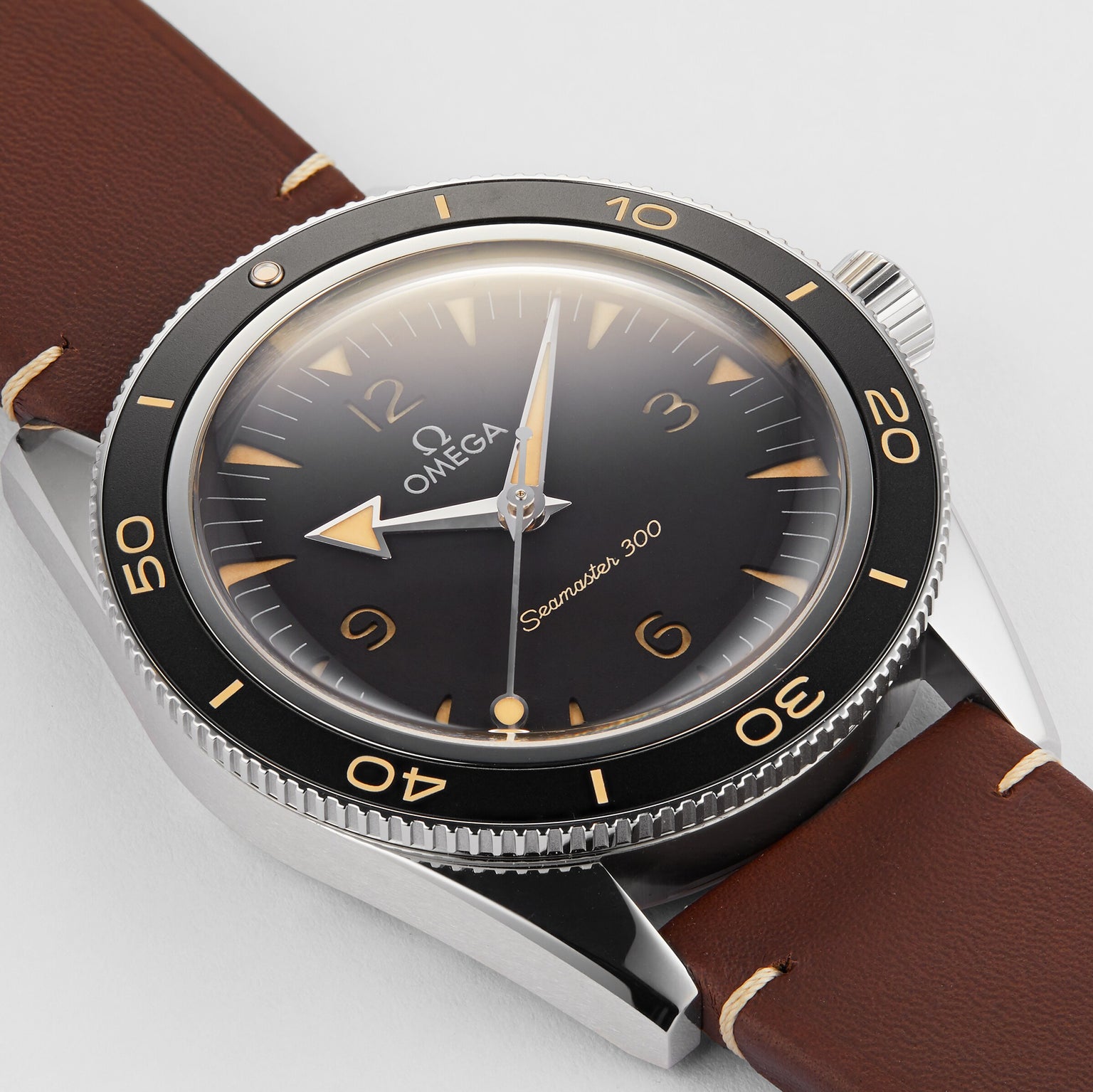 A close-up of the OMEGA Seamaster 300 wristwatch featuring a black dial, vintage-style numerals, brown leather strap, and OMEGA Co-Axial Master Chronometer Calibre 8912 movement.