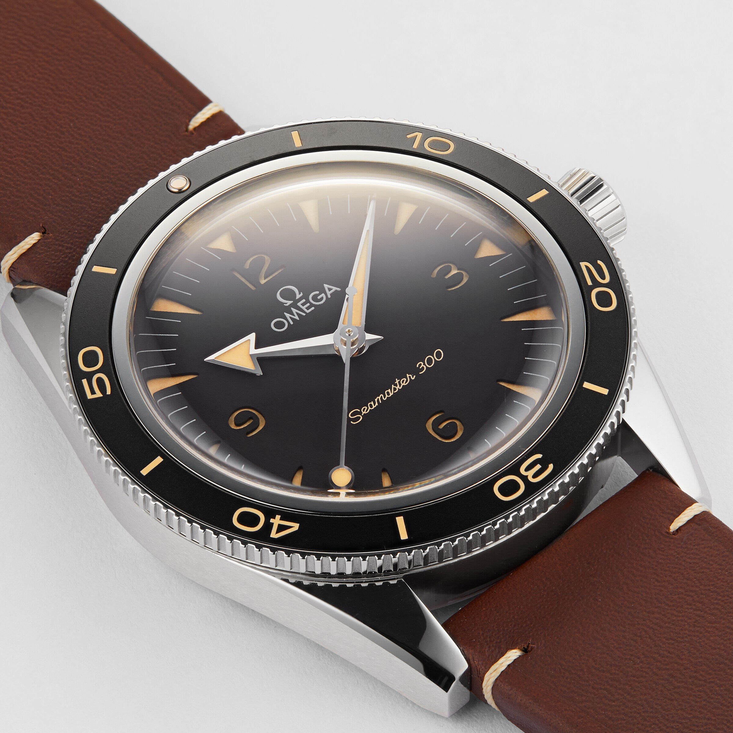 A close-up of the OMEGA Seamaster 300 wristwatch featuring a black dial, vintage-style numerals, brown leather strap, and OMEGA Co-Axial Master Chronometer Calibre 8912 movement.
