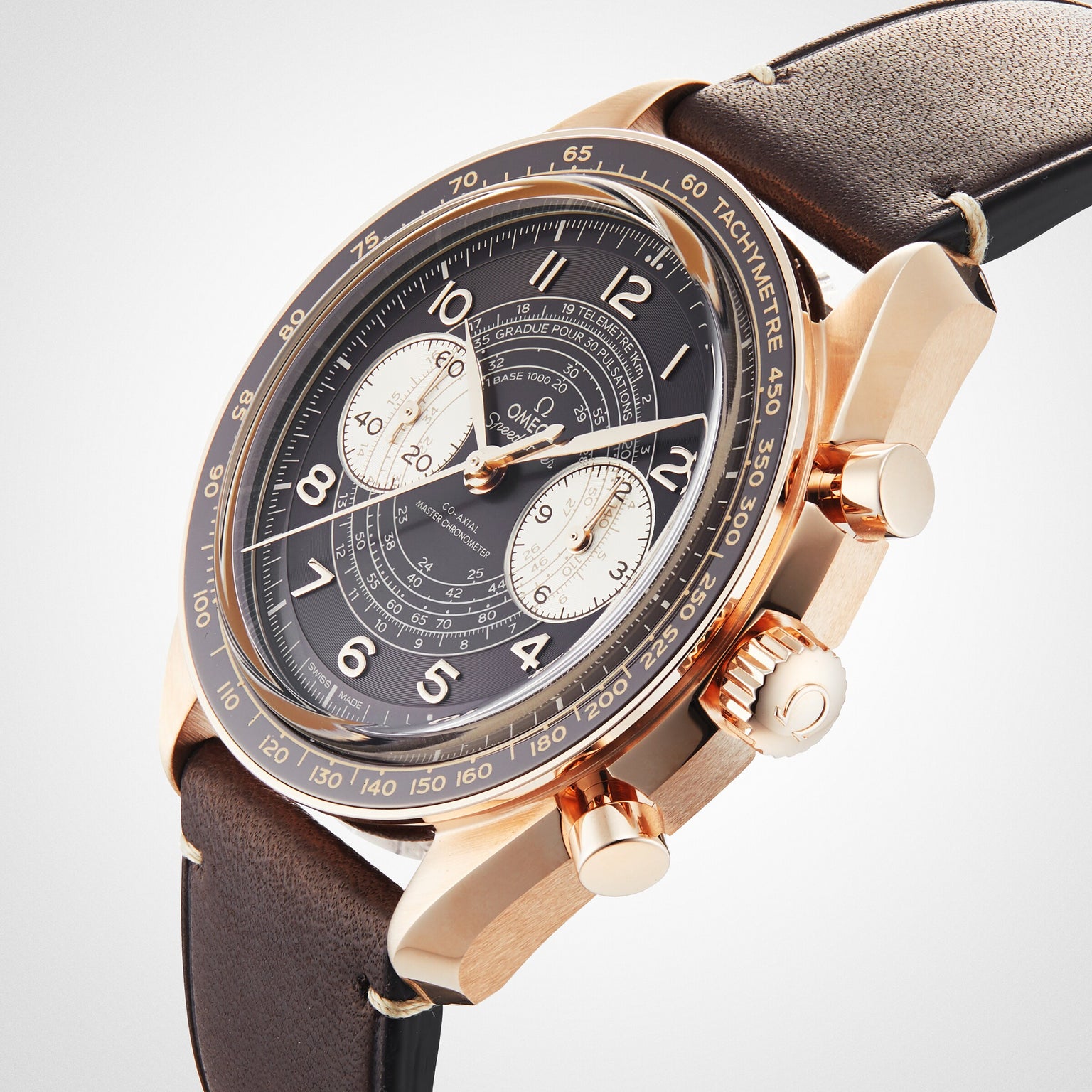 An OMEGA Speedmaster Chronoscope with a gold case, black dial, two subdials, tachymeter scale, and brown leather strap displays its vintage design, positioned at an angle on a white background.
