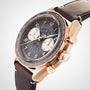 An OMEGA Speedmaster Chronoscope with a gold case, black dial, two subdials, tachymeter scale, and brown leather strap displays its vintage design, positioned at an angle on a white background.