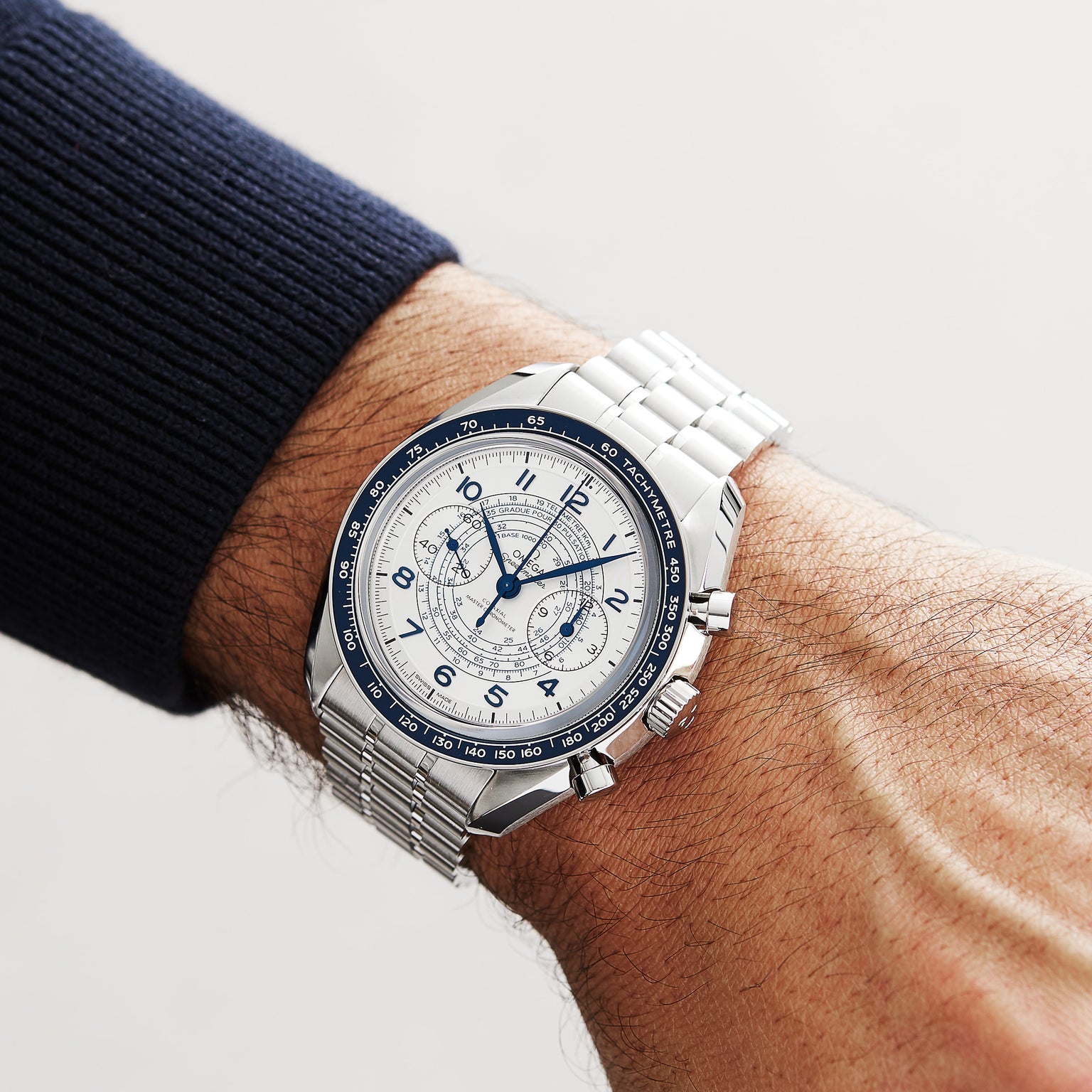 An OMEGA Speedmaster Chronoscope with a blue and white dial is worn on a persons left wrist, displayed against a neutral background.