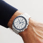 An OMEGA Speedmaster Chronoscope with a blue and white dial is worn on a persons left wrist, displayed against a neutral background.