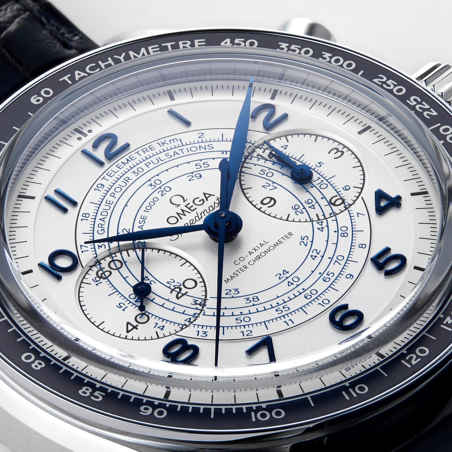 Close-up of the OMEGA Speedmaster Chronoscope, featuring a white dial with blue hands and numerals, tachymeter bezel, 1940s-inspired chronograph sub-dials, and a black leather strap.