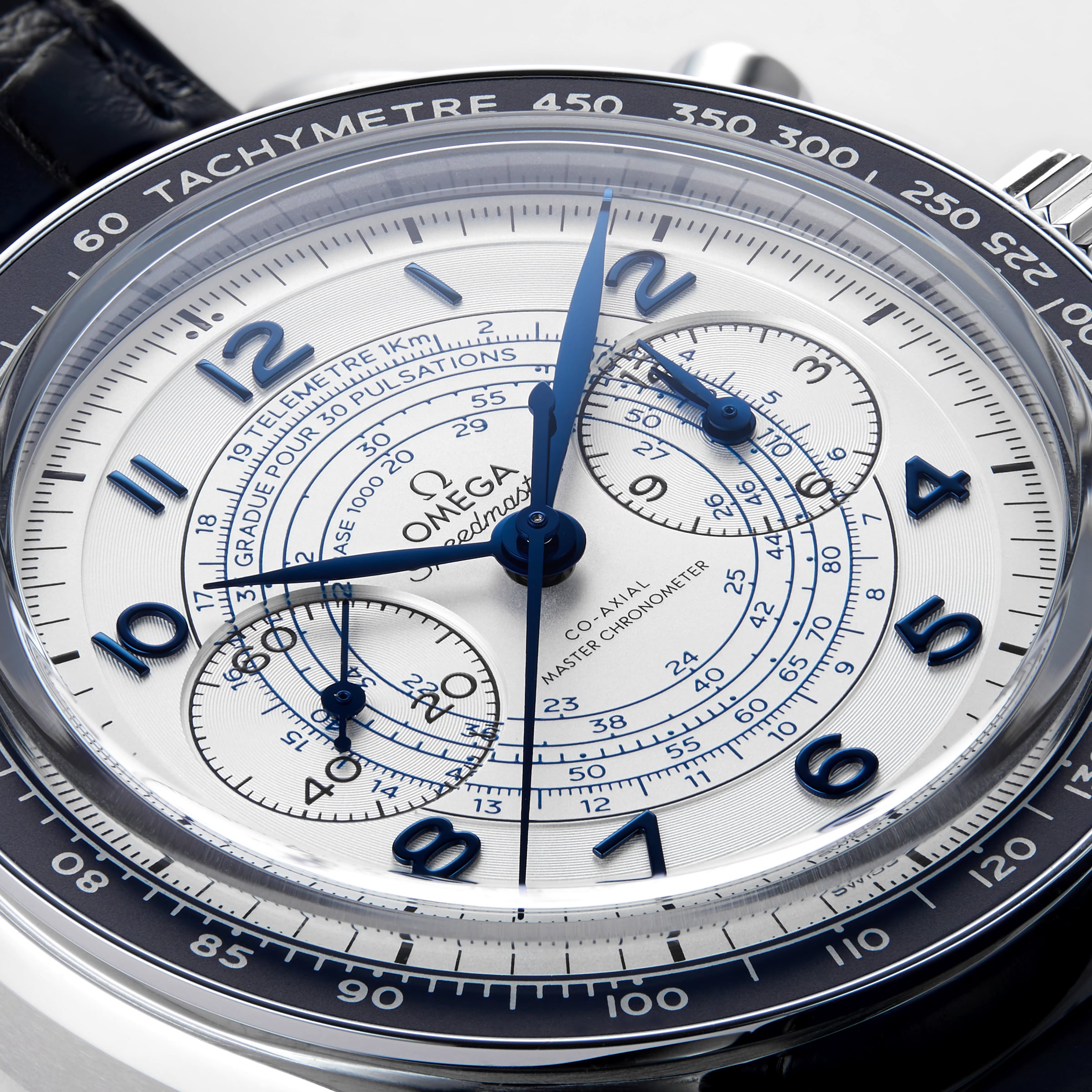 Close-up of the OMEGA Speedmaster Chronoscope, featuring a white dial with blue hands and numerals, tachymeter bezel, 1940s-inspired chronograph sub-dials, and a black leather strap.