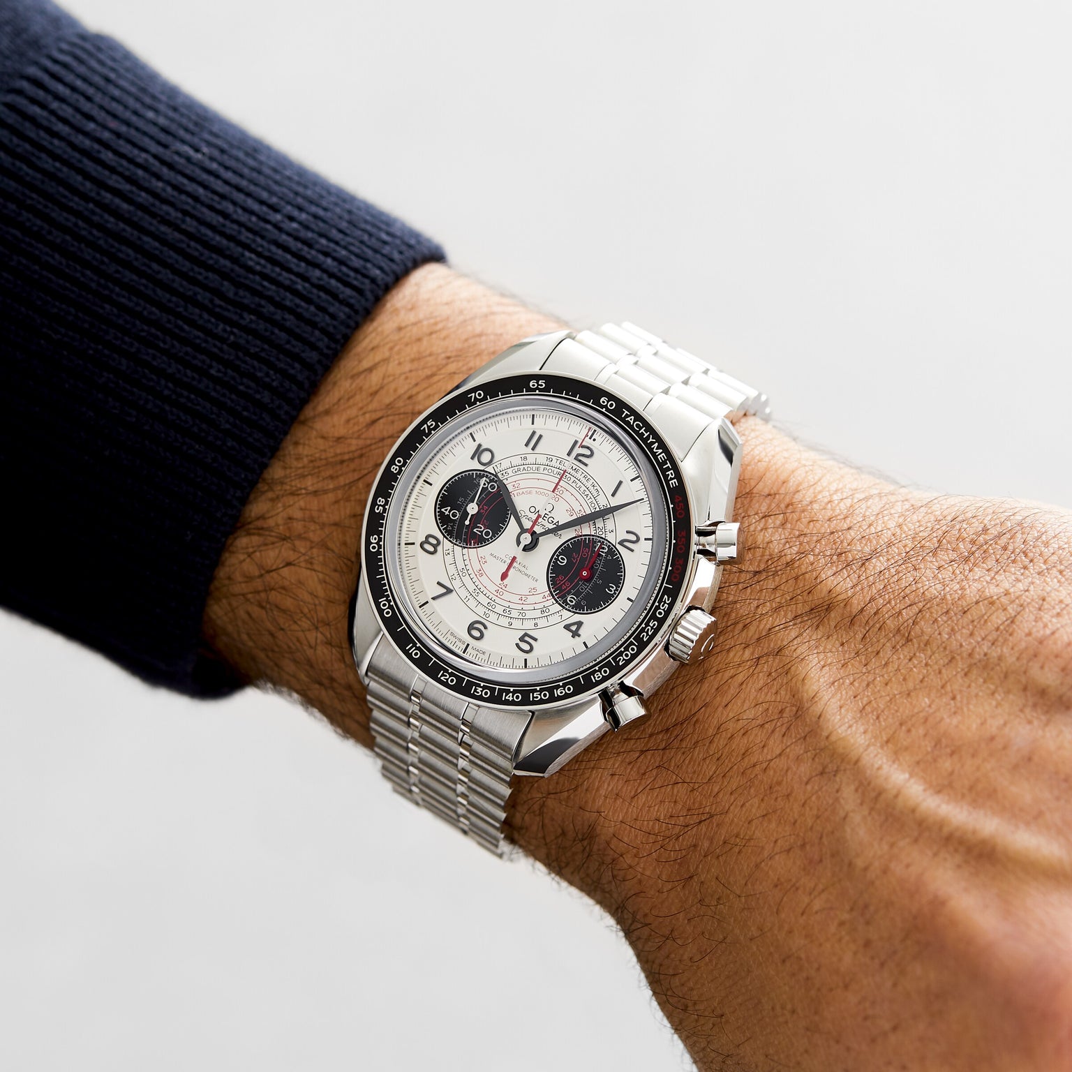 An OMEGA Speedmaster Chronoscope with a white dial, black subdials, and stainless steel bracelet is worn on a persons left wrist.