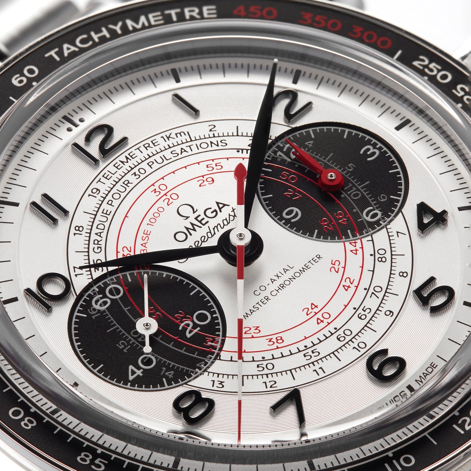 Close-up of the OMEGA Speedmaster Chronoscope watch face with black subdials, red accents, a tachymeter scale, and precise central hands displaying the time.