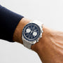 An OMEGA Speedmaster Chronoscope with a blue dial and silver strap is worn on a persons left wrist.