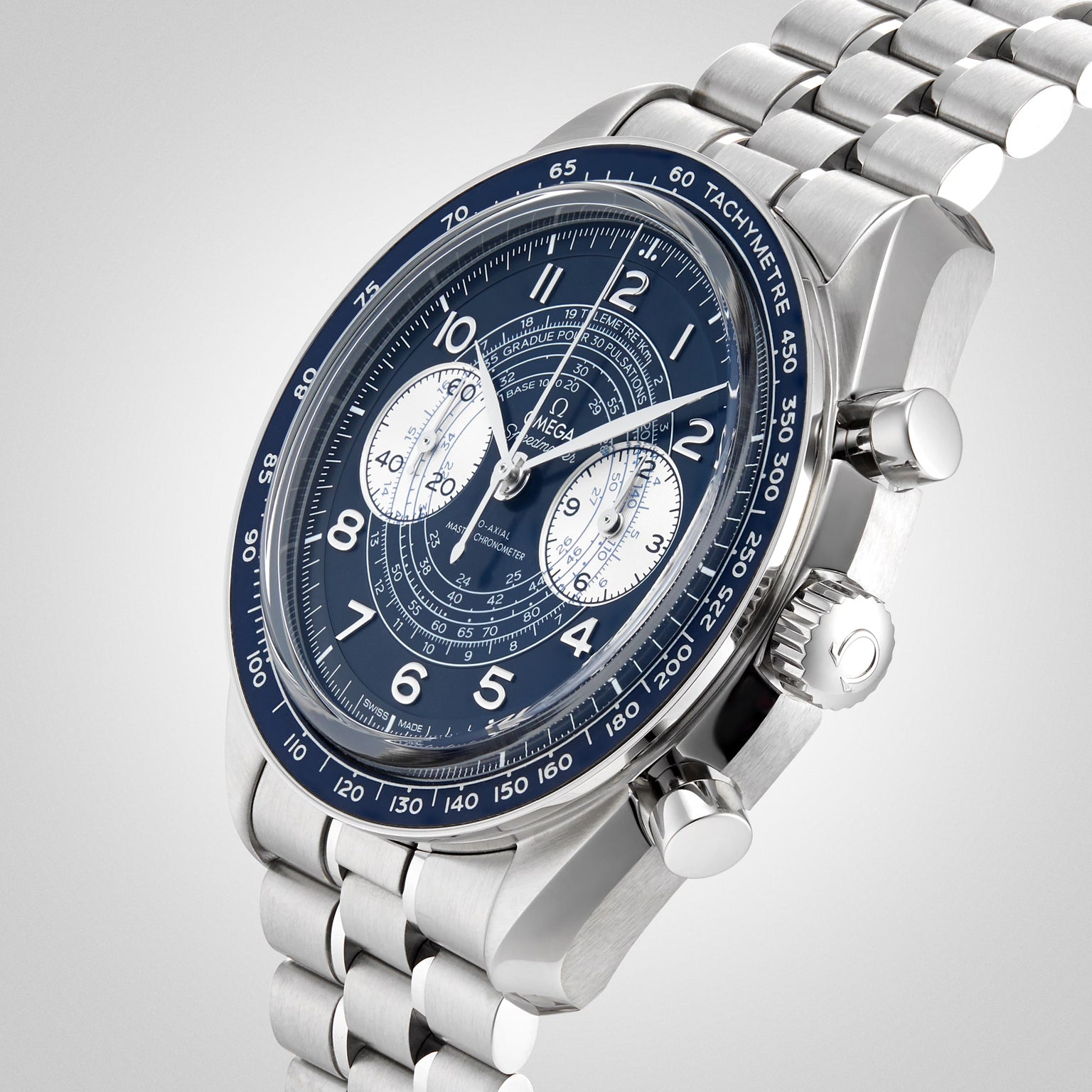 A close-up of the OMEGA Speedmaster Chronoscope, featuring a stainless steel case, blue tachymeter bezel, blue dial with three subdials, and a metal bracelet on a light gradient background.