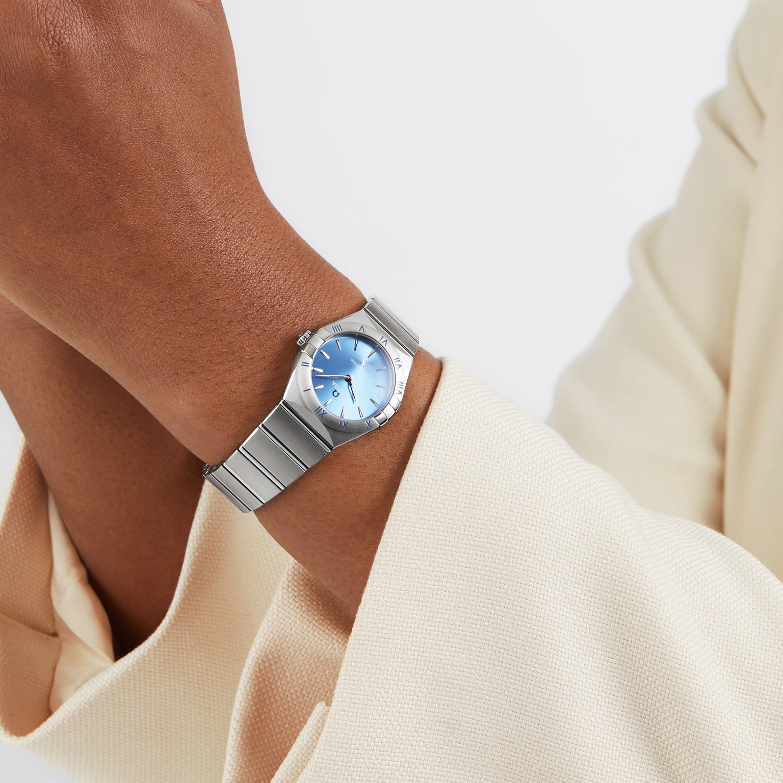A person in a cream-colored blazer wears the OMEGA Constellation, featuring a celestial blue dial and a silver stainless steel case.
