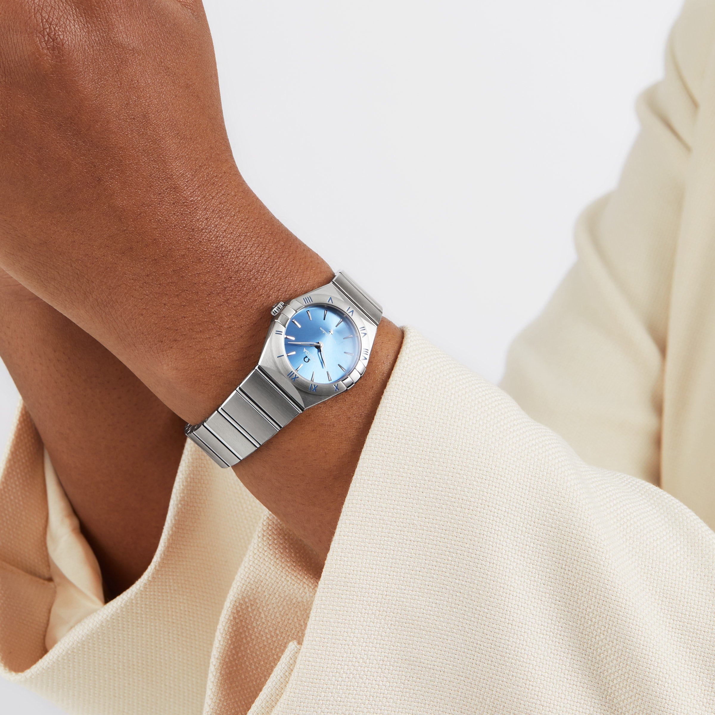 A person in a cream-colored blazer wears the OMEGA Constellation, featuring a celestial blue dial and a silver stainless steel case.