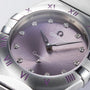 Close-up of the OMEGA Constellation watch showcasing a purple Patchouli blossom dial, diamond hour markers, Roman numerals on the silver bezel, and a stainless steel bracelet.