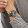 A person wearing a gray sweater and an OMEGA Speedmaster Racing silver chronograph watch with a black leather strap.