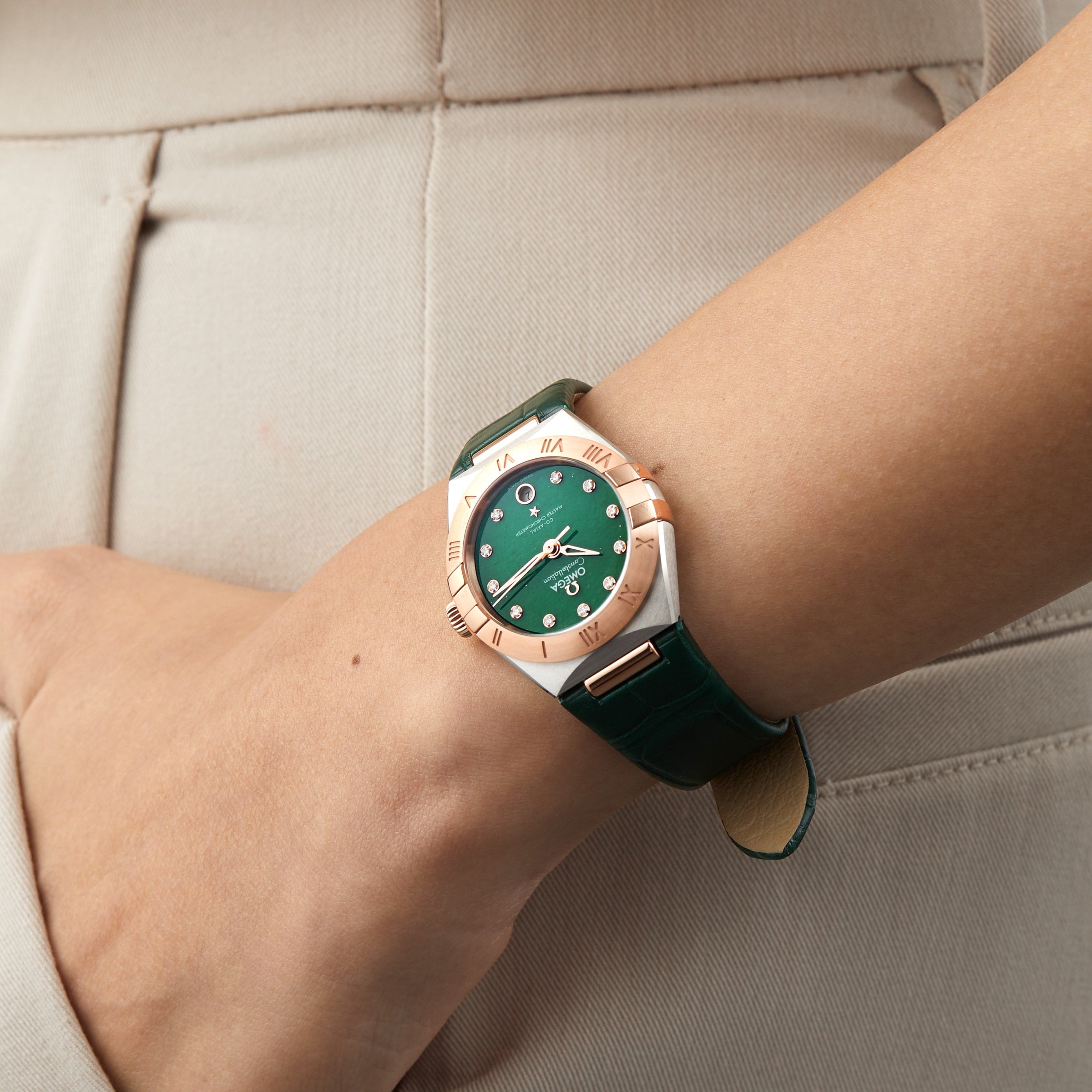 An individual wearing an OMEGA Constellation with 18K Sedna™ gold accents and a leather strap rests their hand on a beige cloth.