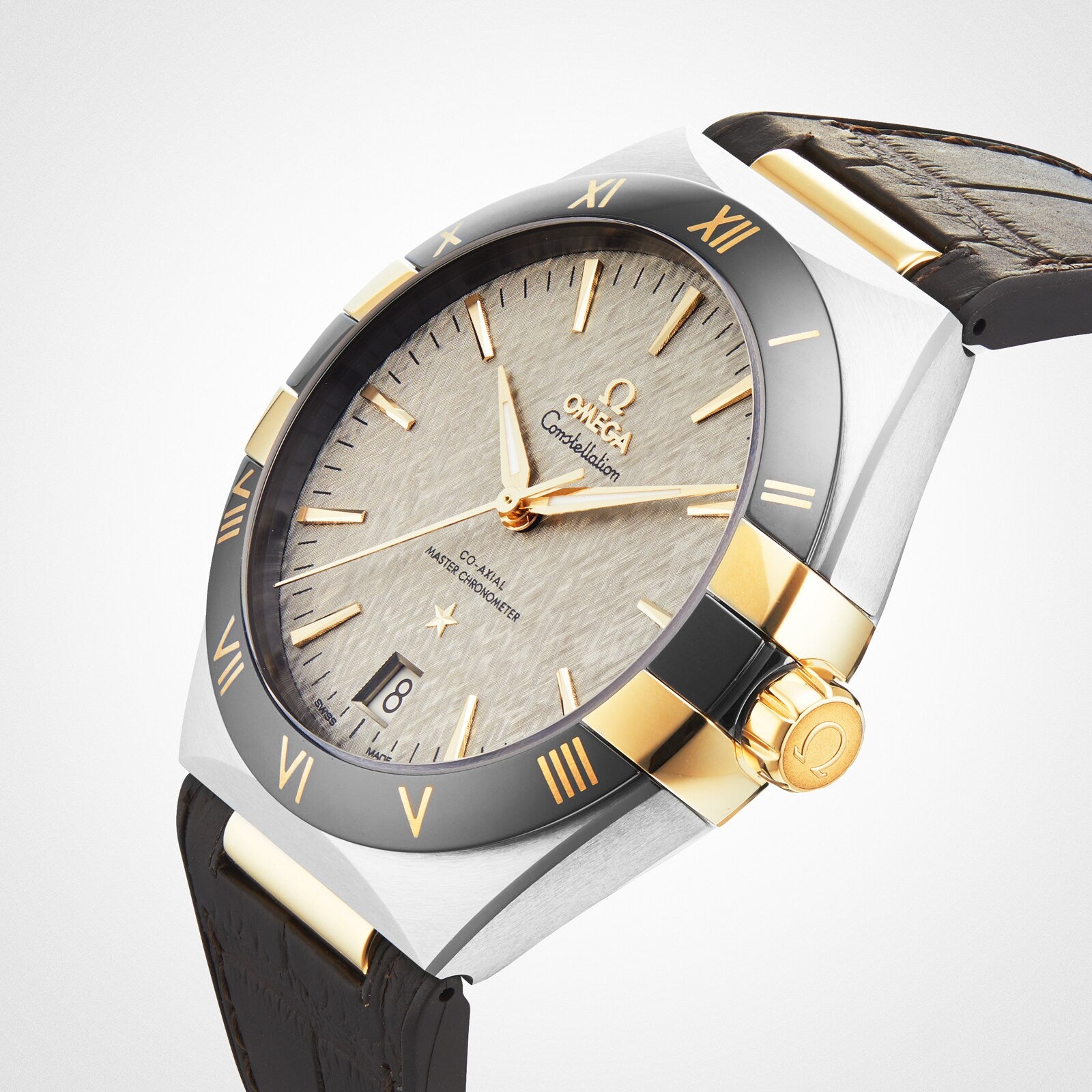 The OMEGA Constellation features a two-tone metal case, black bezel with gold Roman numerals, textured light dial with gold markers, date window, and black leather strap—reflecting classic Constellation heritage.