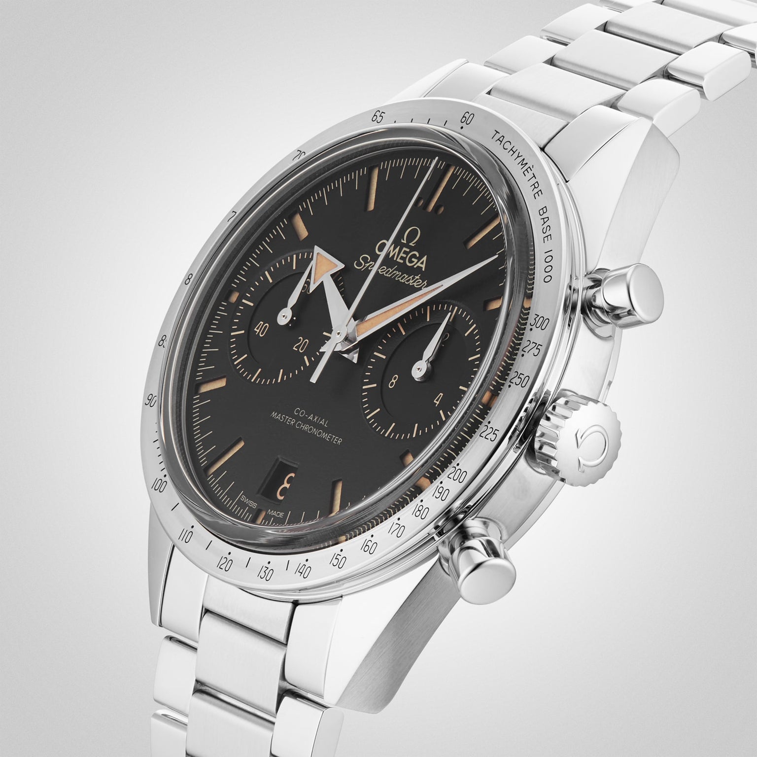 An OMEGA Speedmaster 57 wristwatch with a black dial, three subdials, tachymeter bezel, and stainless steel case is displayed on a matching metal bracelet against a light background.