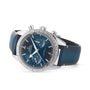 An OMEGA Speedmaster 57 chronograph with a blue dial, blue leather strap, silver bezel, tachymeter scale, and three subdials is shown against a white background.