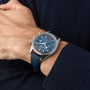 A person wearing an OMEGA Speedmaster 57 chronograph with a blue dial, leather strap, and a dark long-sleeve sweater.