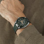 Someone wearing an OMEGA Seamaster Aqua Terra 150M with a textured green strap and green dial, paired with a brown long-sleeve sweater.