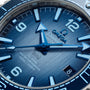 Close-up of the OMEGA Seamaster Planet Ocean 600M Summer Blue watch face, showing blue hands, bold numerals, a date window at 6 oclock, and a 600m/2000ft water resistance mark.