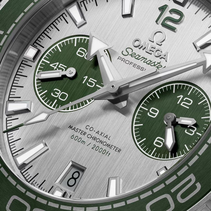 Close-up of an OMEGA Seamaster Planet Ocean 600M watch face, featuring green and silver details, chronograph subdials, date window, Co-Axial Master Chronometer certification, and 600m/2000ft water resistance.