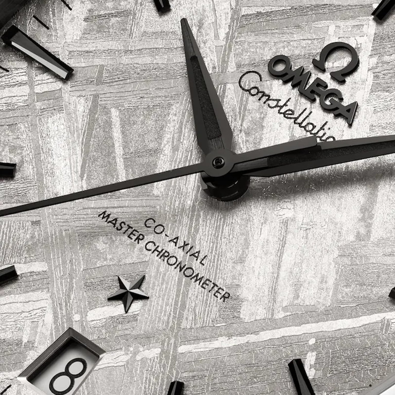 Close-up of an OMEGA Constellation watch face with black hands, meteorite dial, date window at 6 o’clock, and “Co-Axial Master Chronometer” text.