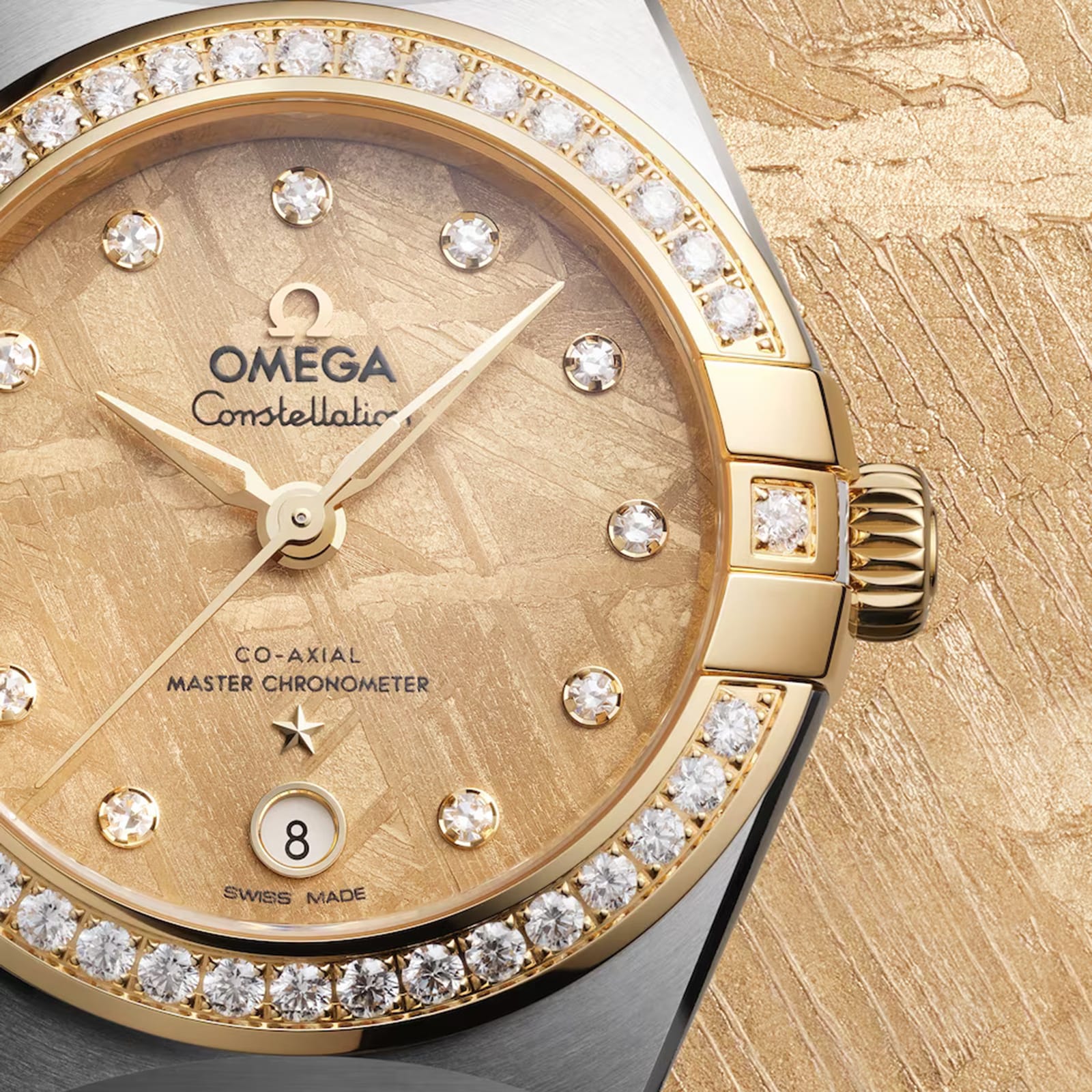 Close-up of the OMEGA Constellation watch featuring a gold meteorite dial, diamond hour markers, diamond-paved bezel, date at 6 o’clock, and powered by the Co-Axial Master Chronometer Calibre 8700, set against a gold textured background.